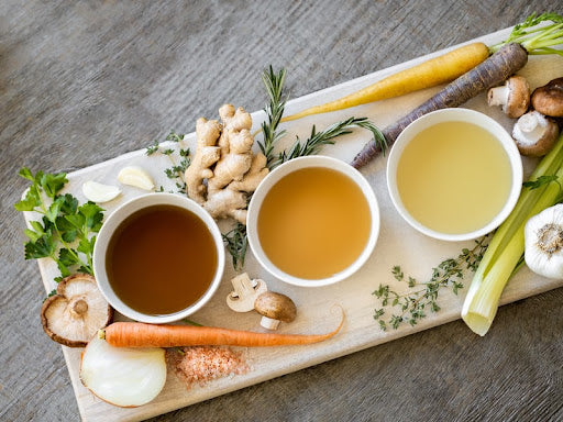 Different types of broth and soups with veggies such as carrots and onions sitting alongside them.
